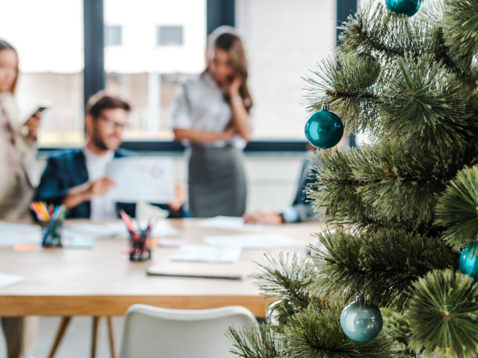 selective focus of decorated christmas tree near multicultural coworkers in office