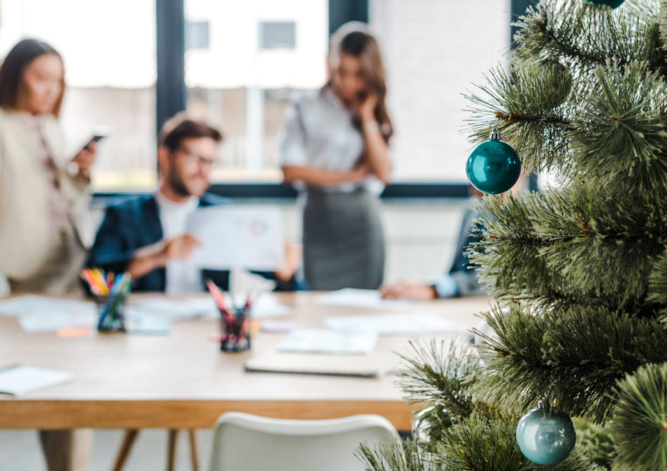 selective focus of decorated christmas tree near multicultural coworkers in office