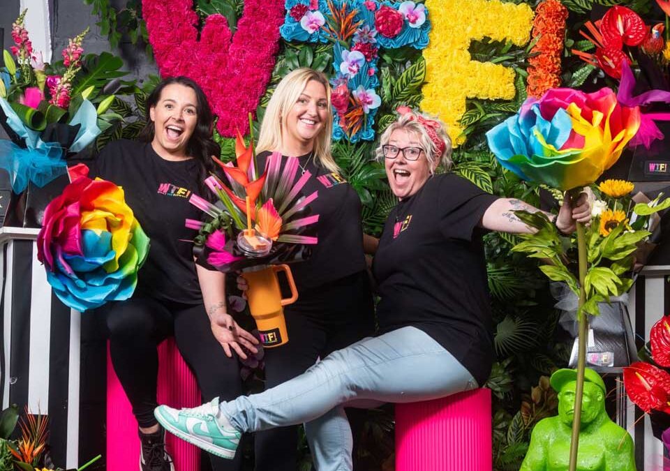 three founders of WTF in front of a vibrant flower display.