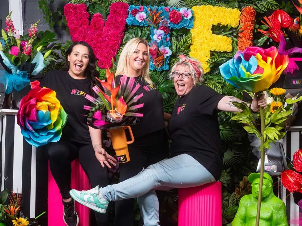 three founders of WTF in front of a vibrant flower display.